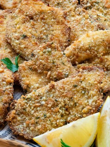 Italian breaded chicken cutlets on a serving platter with lemon wedges on the side.