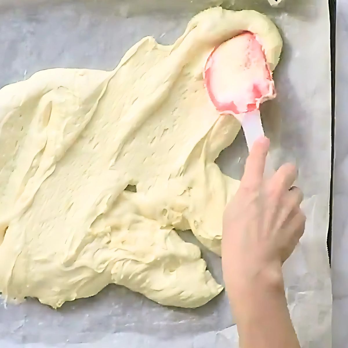 Spreading cake batter on a sheet pan lined with parchment paper.