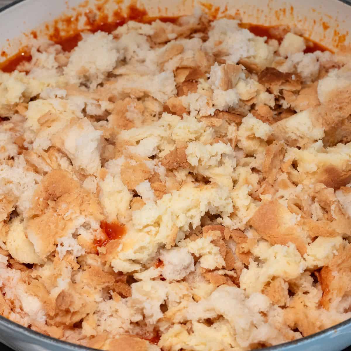 Adding stale bread torn in pieces to the tomatoes in the pot.