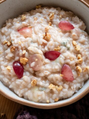 Bowl of creamy grape and gorgonzola risotto garnished with pink grapes and toasted walnuts.