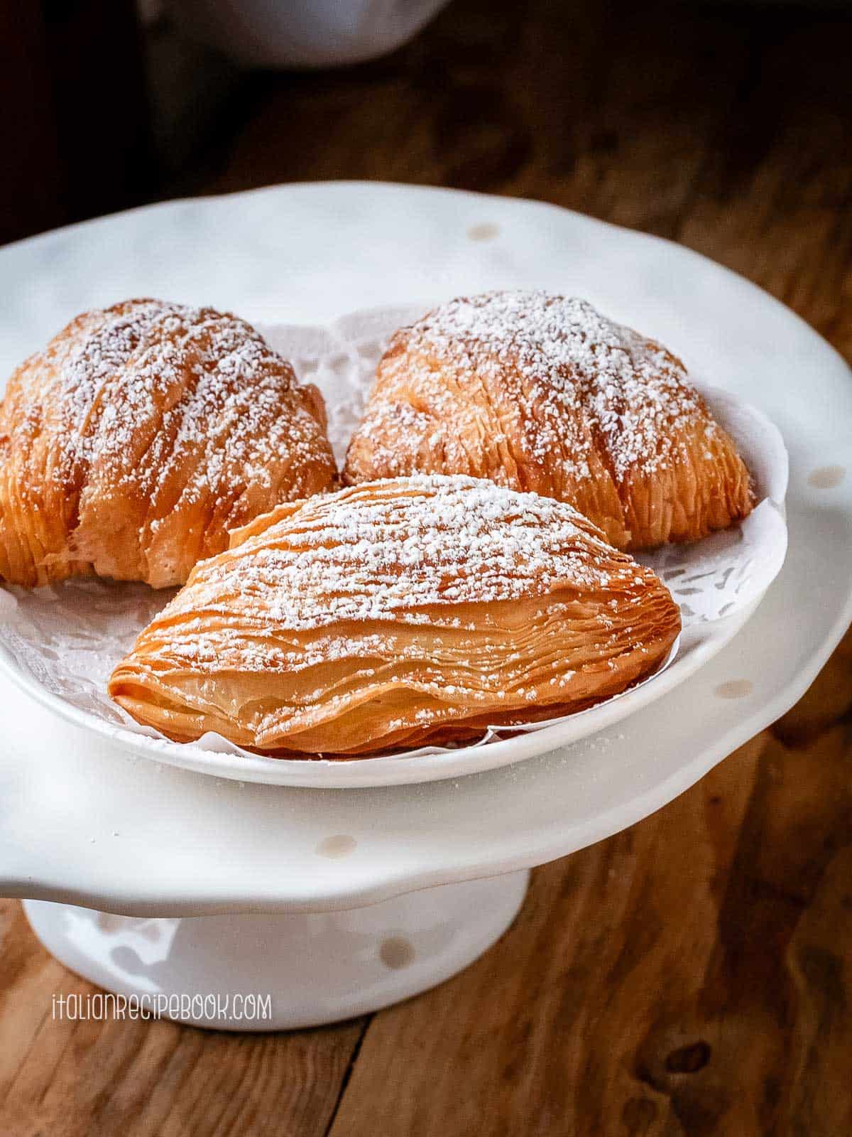 Sfogliatelle dusted with powdered sugar on a dessert stand.