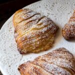 sfogliatelle dusted with confectioners sugar on a white plate