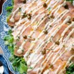 Salmon carpaccio on a serving plate garnished with capers, parsley and lemon zest.