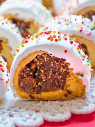 Cuccidati cookies with fig filling topped with icing and sugar sprinkles.