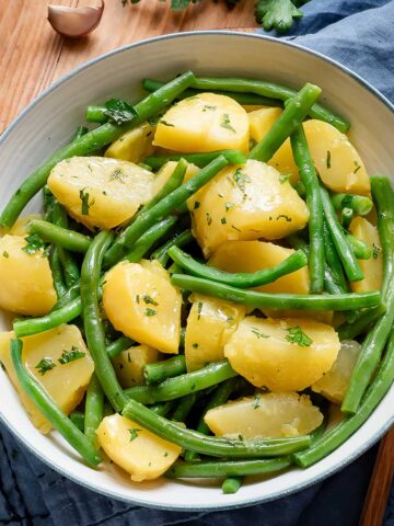 Green beans and potatoes in a white serving bowl with a blue rim.