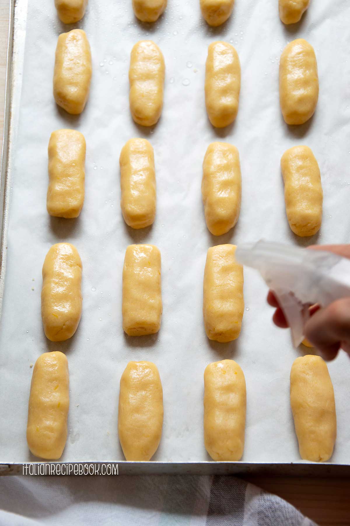 spraying cookies with water to help sesame seeds stick