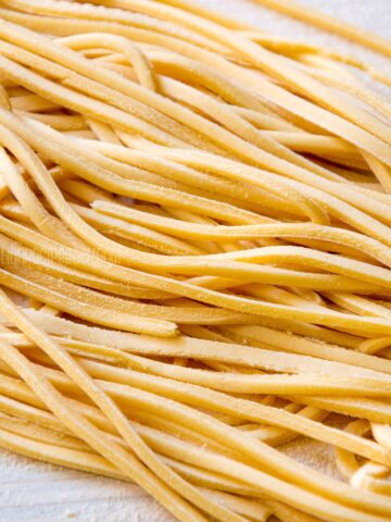 Tonnarelli pasta strands on a wooden board.