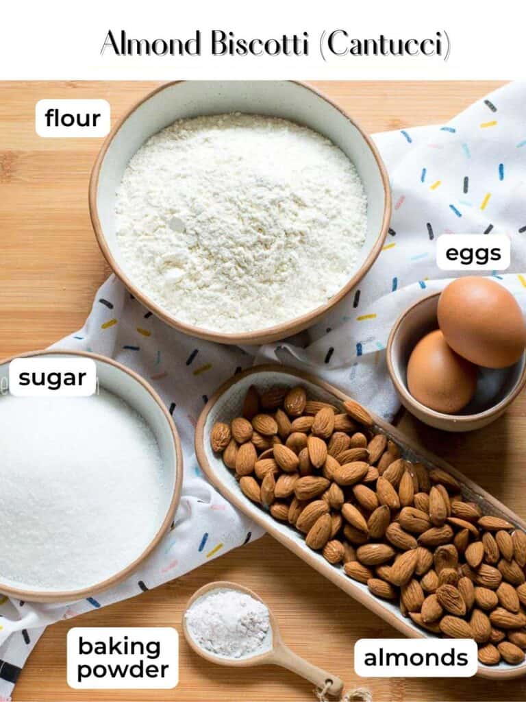 Ingredients needed for cantucci almond biscotti laid on a wooden surface.