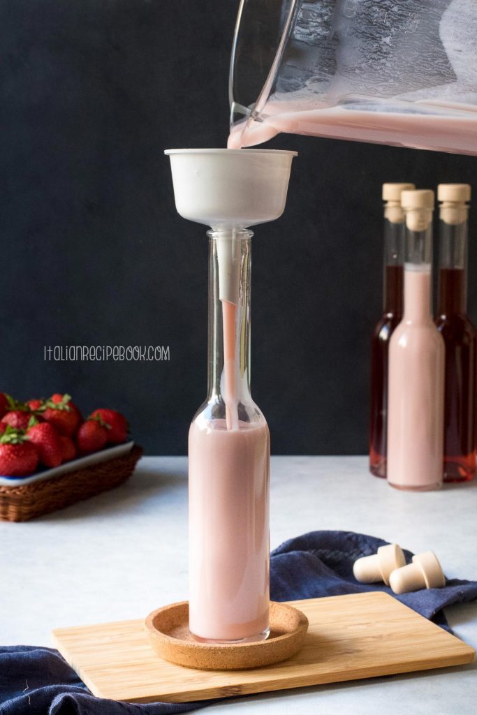 Pouring strawberry cream liqueur in a bottle through a funnel.