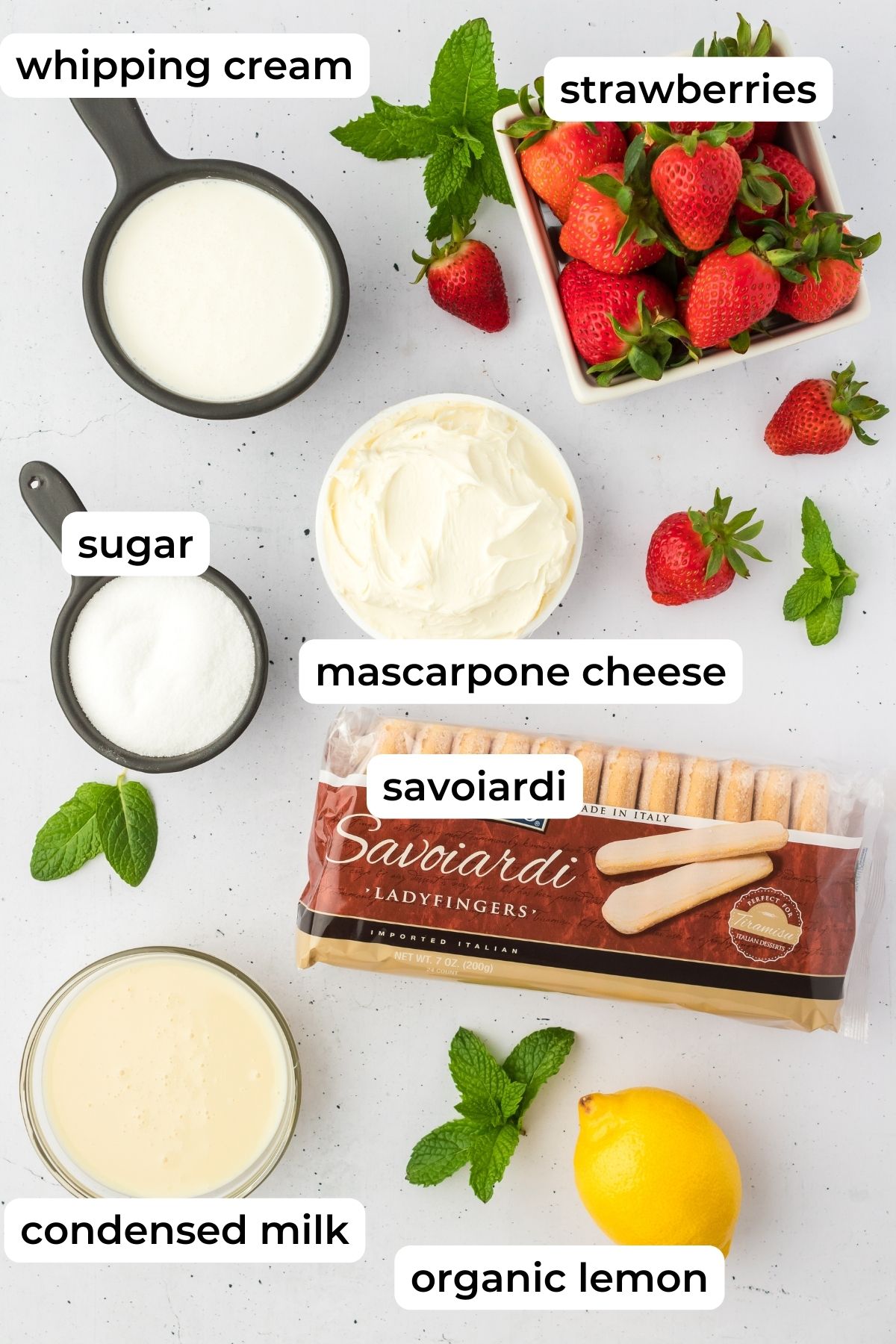 Ingredients needed for strawberry tiramisu laid on white surface.