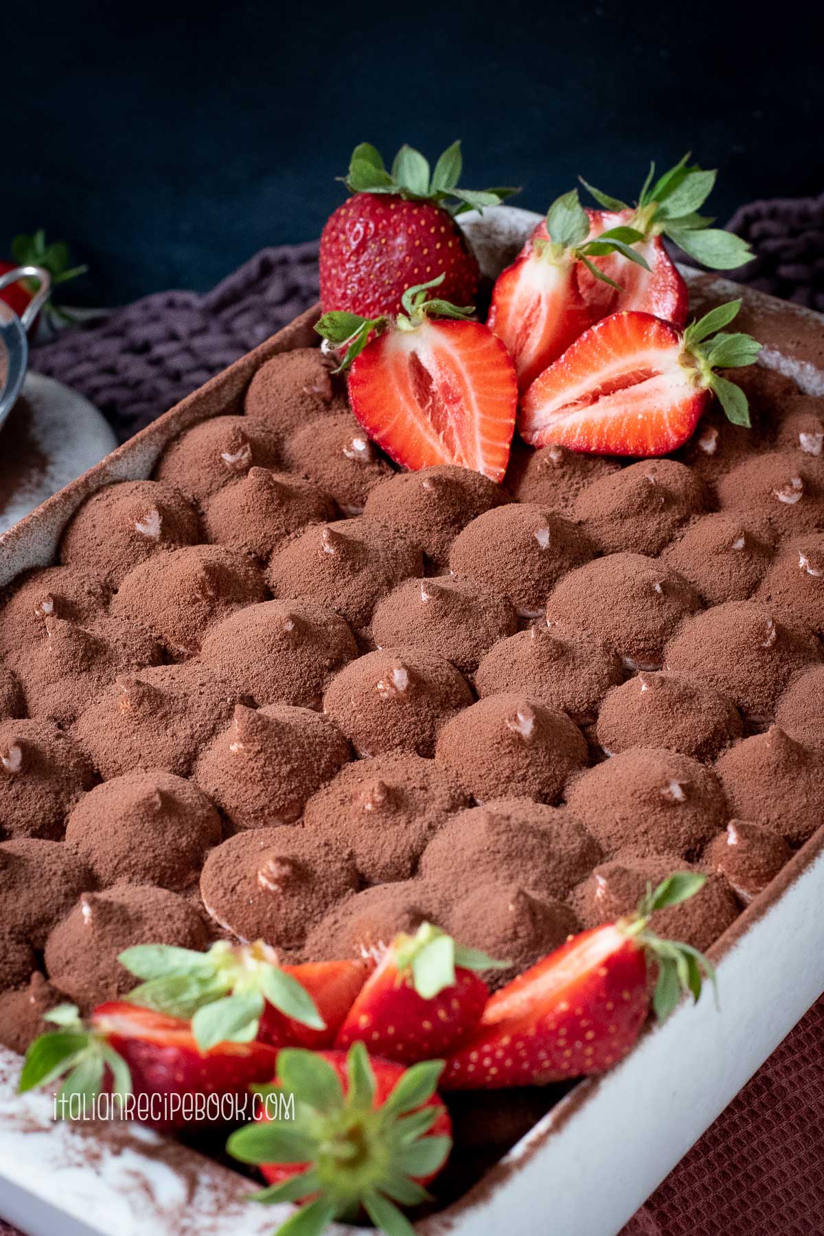 Strawberry tiramisu dusted with cocoa powder and decorated with fresh strawberries.