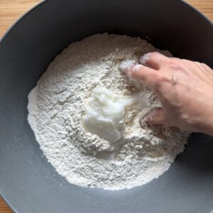 Rubbing cold lard into sifted flour by hand in a large bowl.
