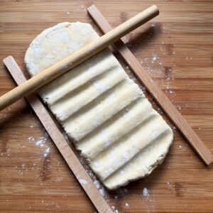 Rolling puff pastry dough into an even rectangle between wooden guide strips with a rolling pin.