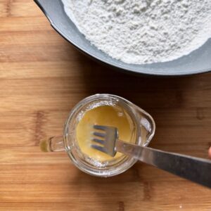 Beating egg with ice-cold water and vinegar with a fork in a glass jug.