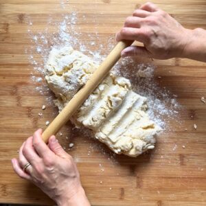 Pressing puff pastry dough log with a rolling pin to flatten it on a wooden board.