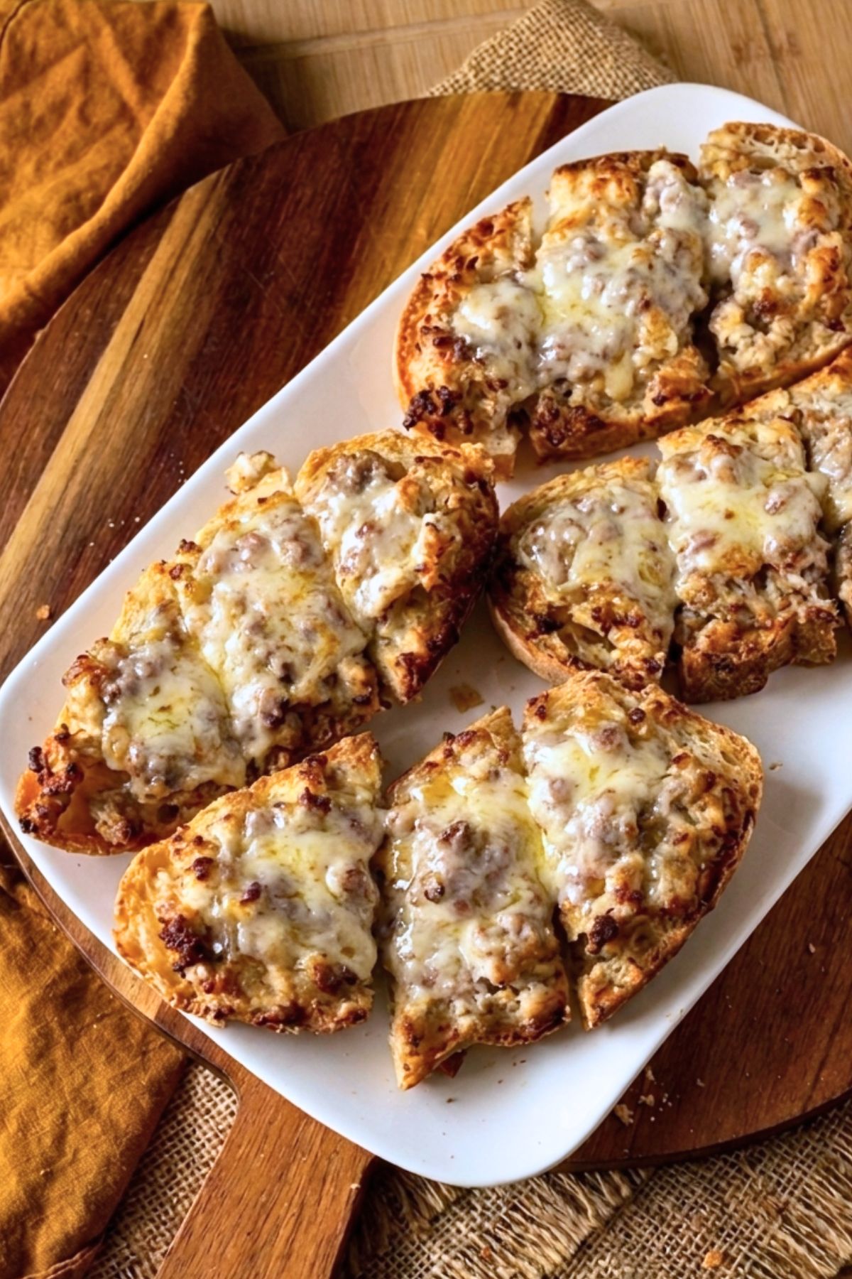 Baked sausage crostone with golden melted cheese topping on a white platter.