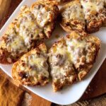 Baked sausage crostone on a white platter.