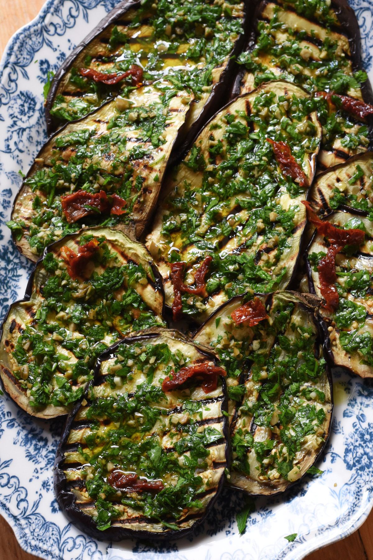 Grilled eggplant steaks on a platter with an olive gremolata sauce and sun-dried tomatoes.