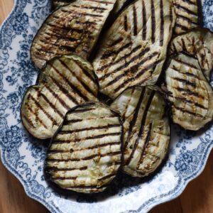 Grilled eggplant steaks with grill marks stacked on a blue and white platter.