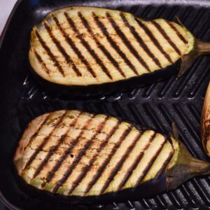 Eggplant steaks grilling with deep char marks on a grill pan.