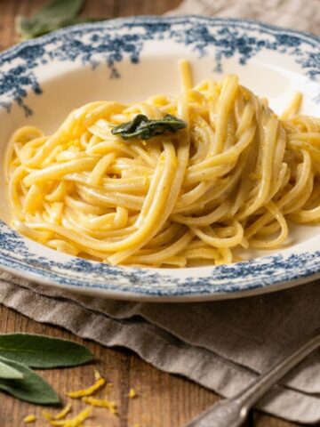 Close-up of creamy lemon linguine pasta al limone garnished with sage in a blue-rimmed bowl.
