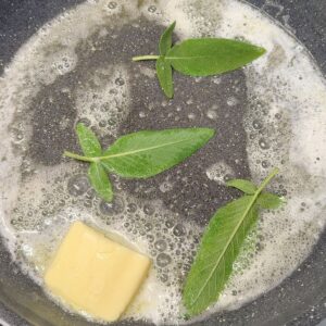 Melting butter with fresh sage leaves in a pan for pasta al limone.