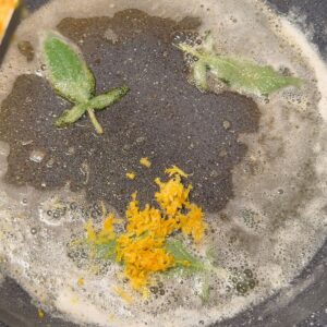 Adding lemon zest to foaming sage butter in a pan for pasta al limone.
