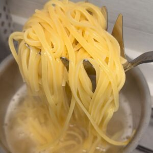 Lifting cooked spaghetti out of the pot on a spider strainer for pasta al limone.