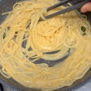 Tossing spaghetti with tongs in the pan to emulsify the pasta al limone sauce.