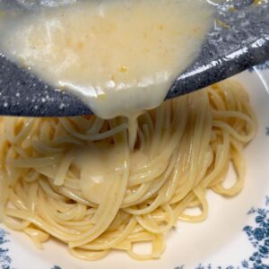 Pouring creamy lemon sauce over a plate of linguine.