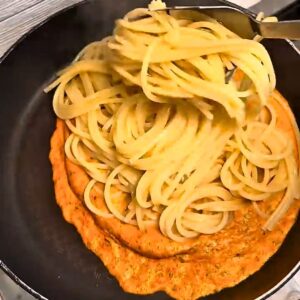 Adding cooked spaghetti to roasted tomato sauce in a pan.