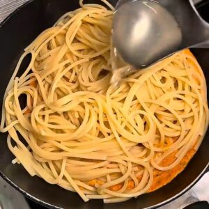 Adding pasta cooking water to spaghetti in a pan.