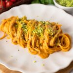 Spaghetti with roasted cherry tomato sauce on a plate and topped with green Parmesan cheese.