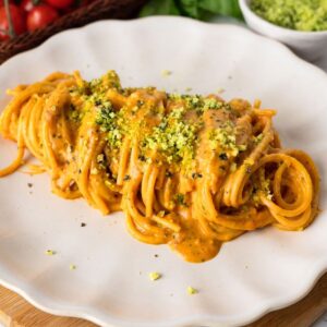 Spaghetti with roasted cherry tomato sauce on a plate and topped with green Parmesan cheese.