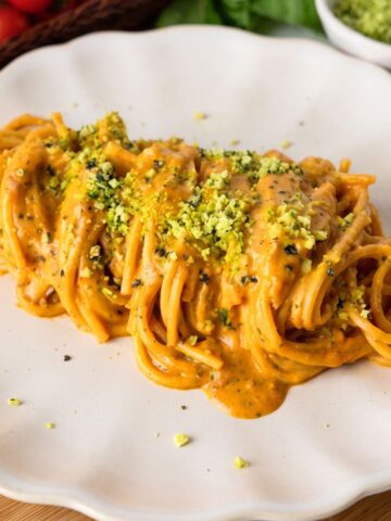 Spaghetti with roasted cherry tomato sauce on a plate and topped with green Parmesan cheese.