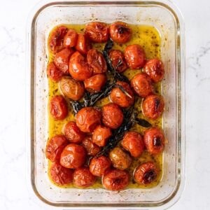 Roasted cherry tomatoes with basil and garlic in olive oil in a glass container.