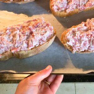 Rustic bread topped with a thick layer of raw sausage and cheese on a baking tray going in the oven.
